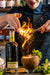 Bartender With Rum Bottle And Fire Over A Cocktail